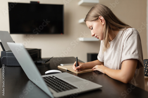 Cute focused girl does work from home  writes notes in a notebook during quarantine and pandemic.