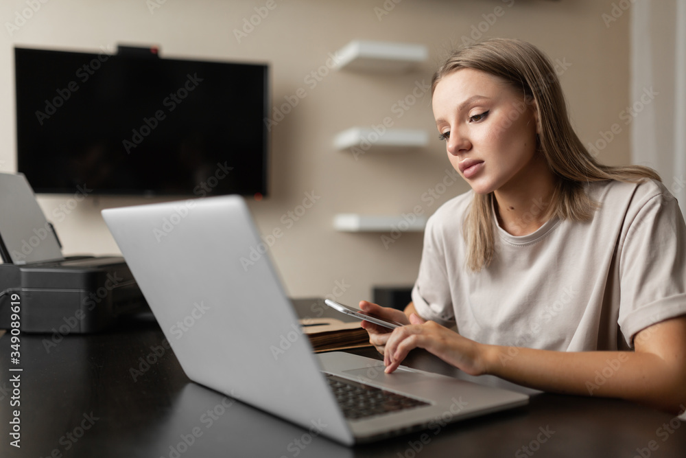 A cute pensive girl does work from home, scans information on the phone and checks it against information on the computer during quarantine and pandemic. A cute pensive girl does work from home, scans information on the phone and checks it against information on the computer during quarantine and pandemic.