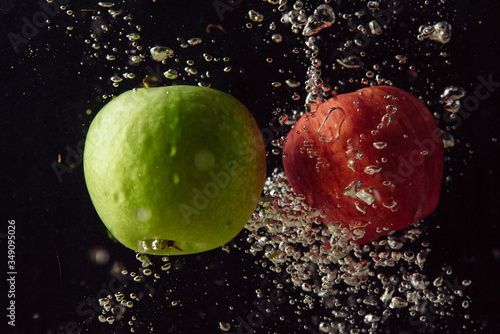 Green and red apple fruits falling into water and splashing against black background