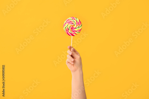 Hand with sweet lollipop on color background