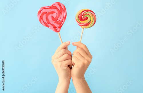 Hands with sweet lollipops on color background