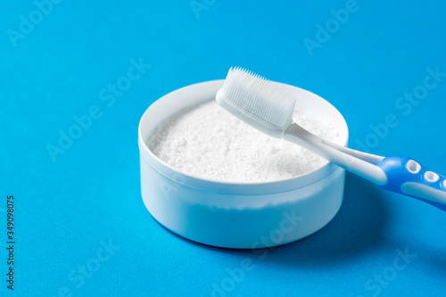 A toothbrush with white silicone bristles on a jar of tooth powder.