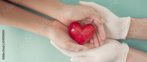 Fototapeta Naklejka Na Ścianę i Meble -  Doctor hands with medical gloves holding child hands and red heart, health insurance, donation, charity during covid-19 coronavirus pandemic, saving life, thank you and appreciation to doctor