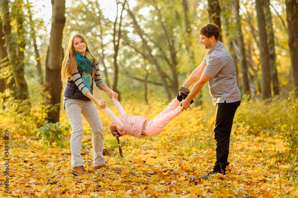 Fototapeta premium Father mom and their daughter have fun together. Parents hold their daughter's arms and legs and cheerfully throw her up.