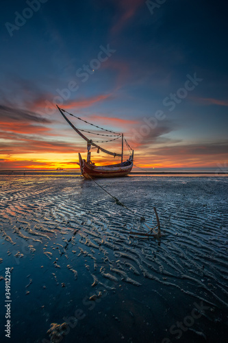 Indonesia traditional wooden ships and beautiful sand beach. Traditional Sasaknese boat Jukung at Mlandingan beach, Situbondo. Fisherman boat on the beach at sunset sky. photo