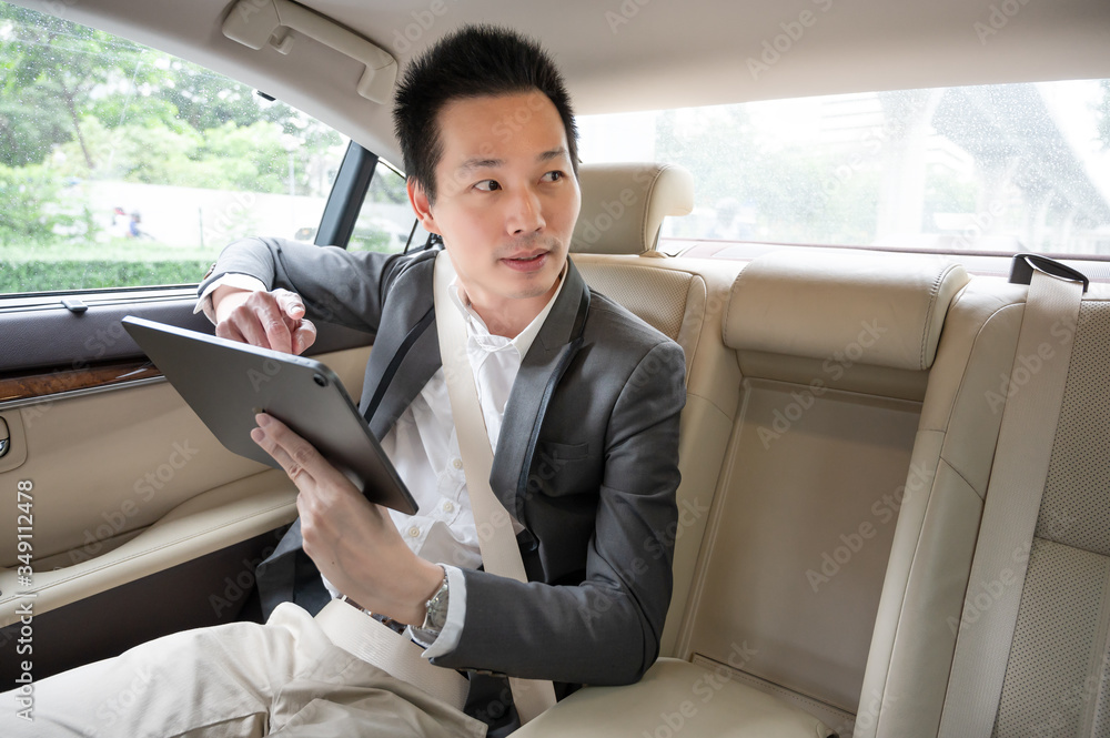 Young asian businessman using tablet and looking out of window while sitting on the back seat in the car. hurrying to work. Young asian businessman using tablet and looking out of window while sitting on the back seat in the car. hurrying to work.