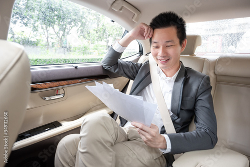 Young asian businessman looking at many financial documents and Satisfied with the operating results while sitting on the back seat in the car. 