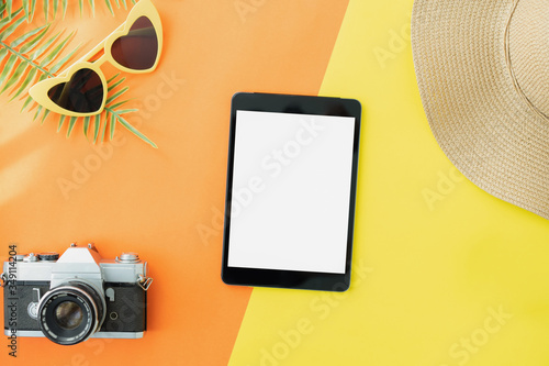 Top view of black digital tablet and hat with camera on orange color background. Summer holiday and travel concept..