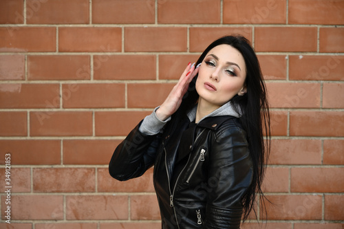 Close-up portrait in spring weather outdoors caucasian fashionable brunette girl in black jacket. Model posing against the backdrop of a building wall.
