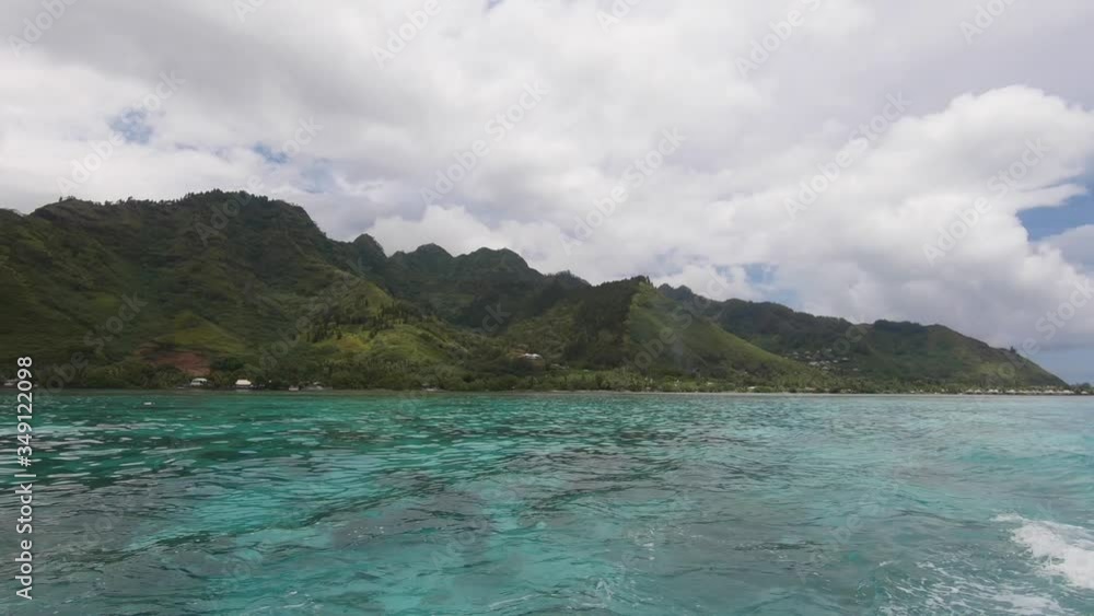 A view of Moorea Island, Tahiti, green lush mountains, clear blue water, boat wake A view of Moorea Island, Tahiti, green lush mountains, clear blue water, boat wake