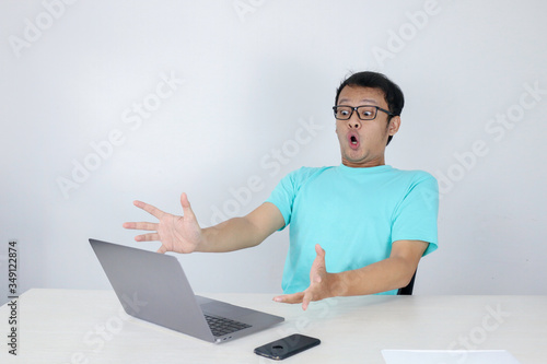 Wow face of Young Asian man shocked what he see in the laptop when working isolated grey background wearing blue shirt.