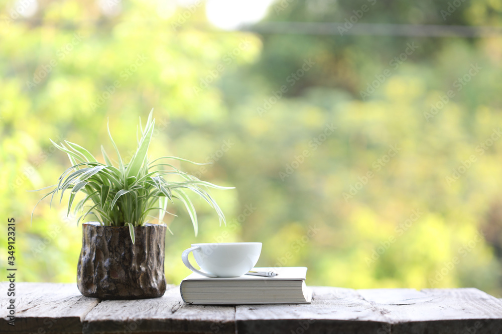 notebook and white coffee cup with plant in small wooden pot on wooden table at outside notebook and white coffee cup with plant in small wooden pot on wooden table at outside