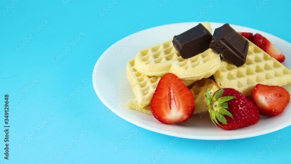 Waffles on plate with two chocolate cubes and strawberries on blue background Waffles on plate with two chocolate cubes and strawberries on blue background