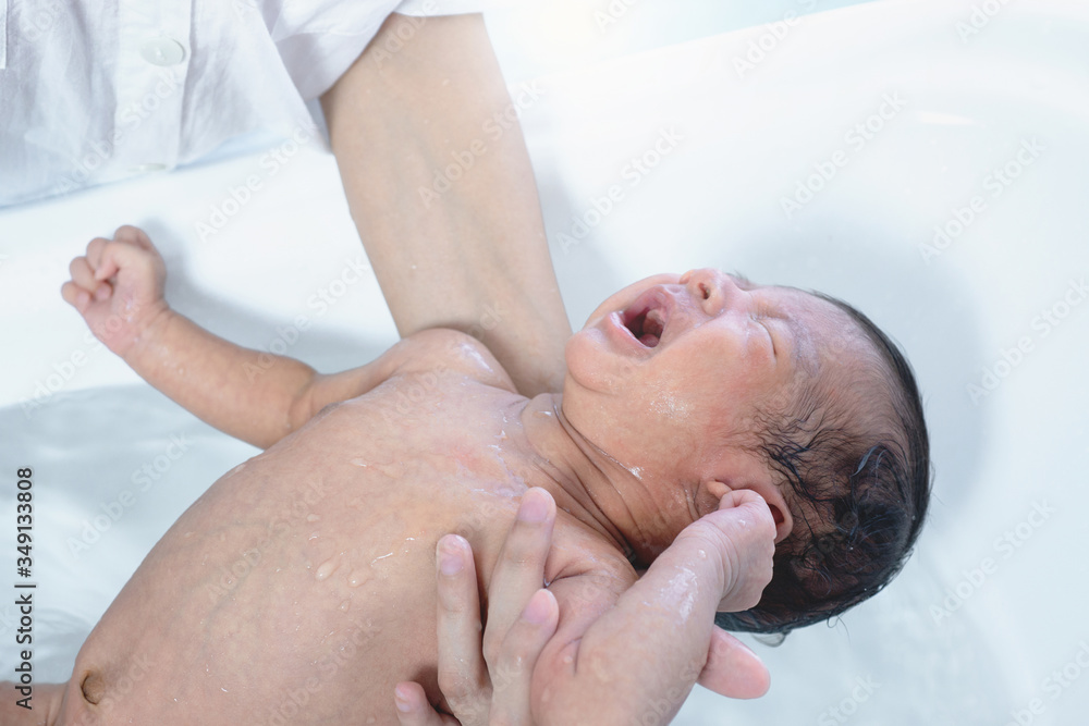 Bathing a cute Asian newborn baby with a yellow sponge and cried loudly, safe in mother's arms, newborn baby concept Bathing a cute Asian newborn baby with a yellow sponge and cried loudly, safe in mother's arms, newborn baby concept