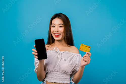 Portrait of happy Asian pretty girl holding smartphone and credit card for presenting online shopping isolated over blue background,colorful shopping concept.