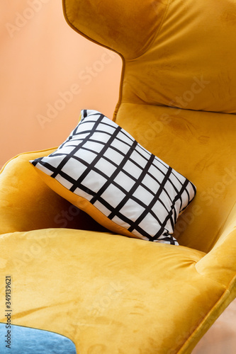 Yellow velvet cosy armchair with double-sided pillow with striped pattern in close-up.
