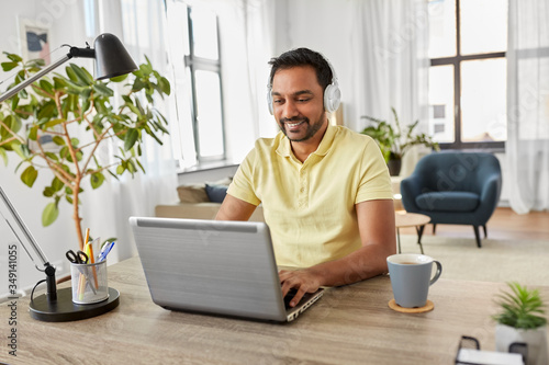 remote job, technology and people concept - happy smiling young indian man in headphones with laptop computer working at home office