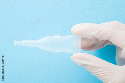 Doctor hand in white rubber protective gloves holding plastic tube of rotavirus vaccine for babies health on light blue table background. Pastel color. Closeup. Medical concept.