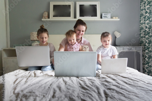 Mom and Three children sitting on bed with laptops