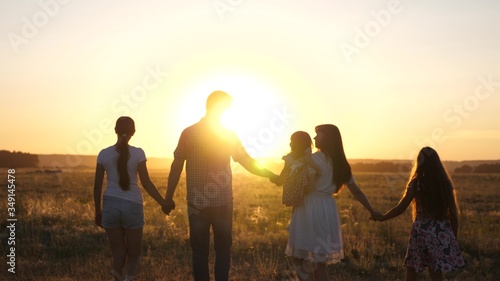 free Happy family walks in field in sunset light. healthy dad mom and daughters walk in park in sunshine. children and parents travel on vacation. happy father carries a child. happy childhood concept