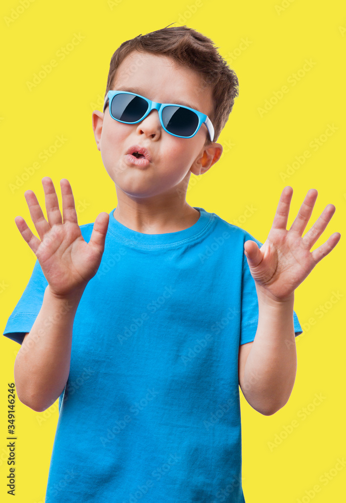 Little boy in sunglasses raised his hands up, on yellow background Little boy in sunglasses raised his hands up, on yellow background