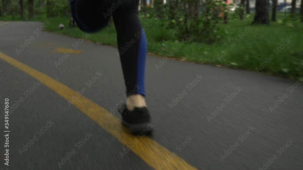Female runners feet running on wet footpath in city park after rain
