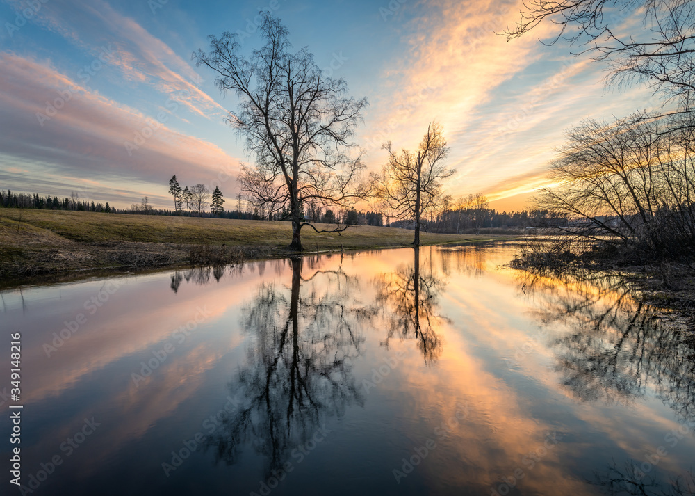 Beautiful sunset glow with calm landscape with tree reflections and sunlight at spring evening in river Finland Beautiful sunset glow with calm landscape with tree reflections and sunlight at spring evening in river Finland
