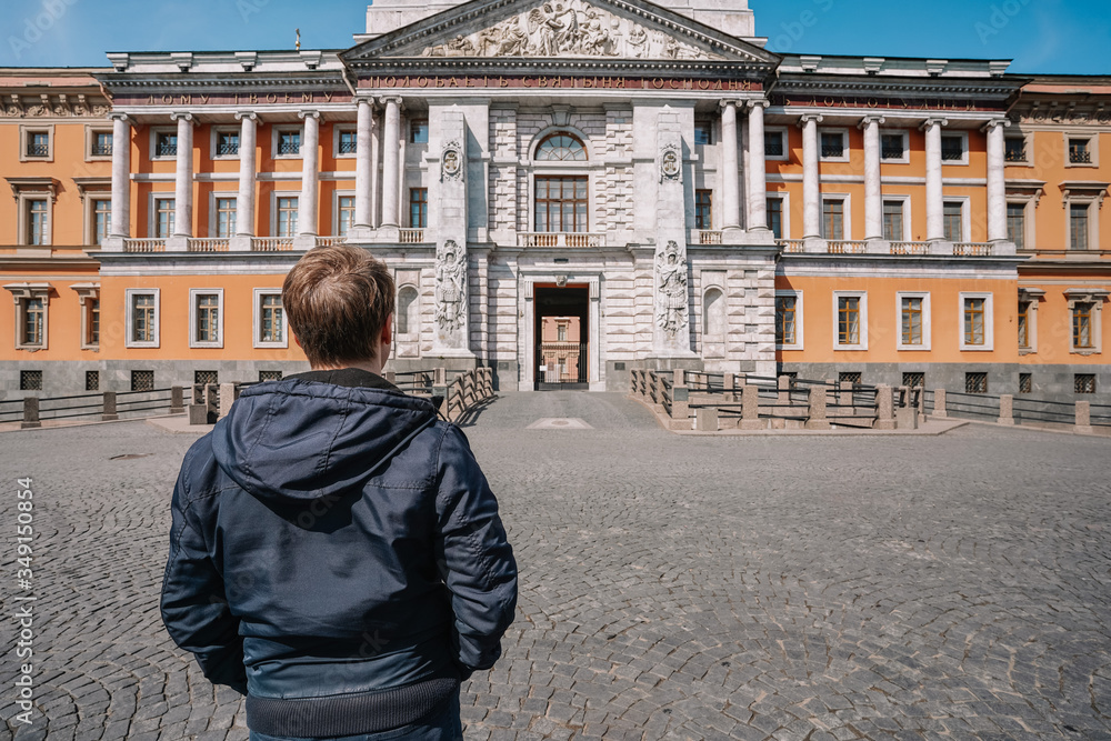 Portrait of a young man in a jacket and with a backpack on the background of an architectural monument, a historical castle in Saint Petersburg