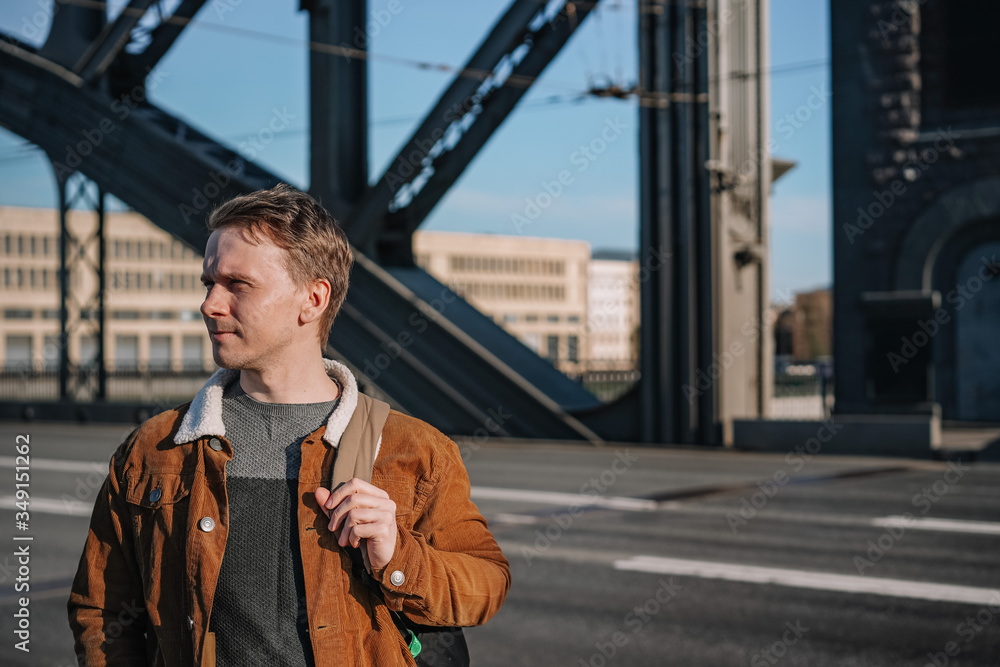 A business man in a beige jacket and with a backpack walks in Sunny weather on the beautiful drawbridge over the Neva river in St. Petersburg, an architectural monument, a metal bridge with towers A business man in a beige jacket and with a backpack walks in Sunny weather on the beautiful drawbridge over the Neva river in St. Petersburg, an architectural monument, a metal bridge with towers