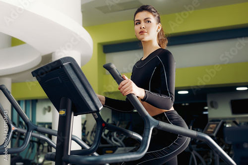 Young brunette girl, in black training leggings and long sleeve top engaged on treadmill in the gym. Free space for text, concept of fitness club