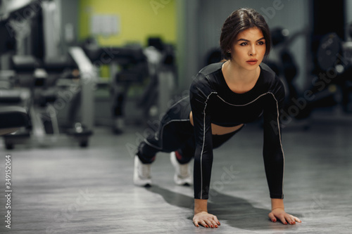 Young brunette in black sweatpants and a long sleeve top doing fitness in the gym. Free space for text. Close up and vertical photo, fitness club concept