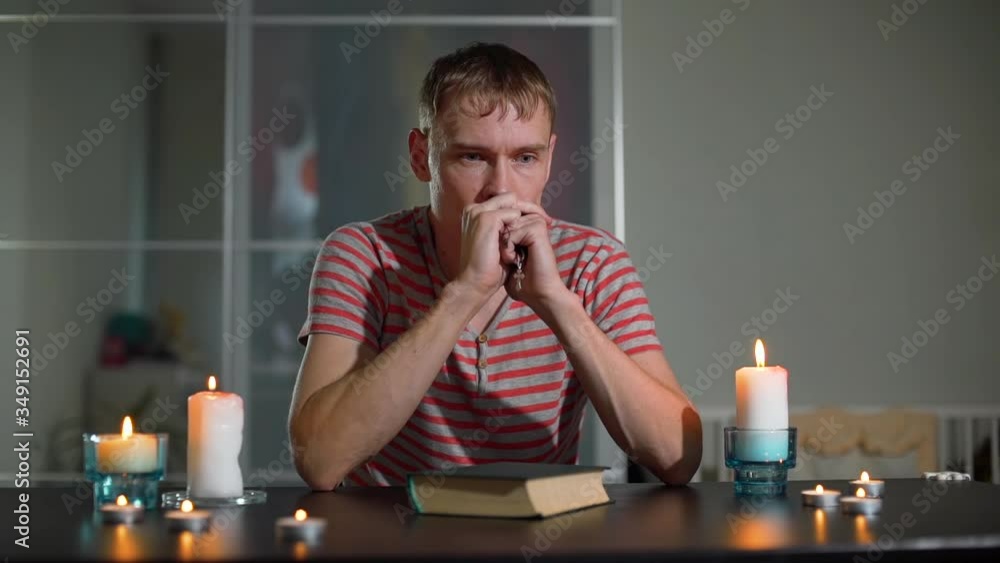 Religious Young Man Folding Hands in Prayer at Home. He is Holding Rosary with Cross in his Hands. Slow Motion. Faith, Spirituality and Religion Concept Religious Young Man Folding Hands in Prayer at Home. He is Holding Rosary with Cross in his Hands. Slow Motion. Faith, Spirituality and Religion Concept