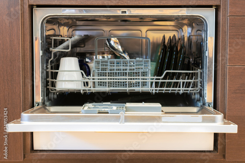 Open dishwasher with clean dishes. built into the kitchen