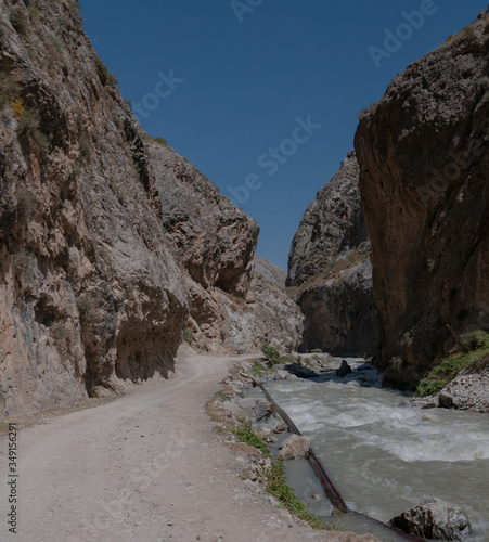 mountains of Central Asia. a narrow road between mountains. rapid river and sparse vegetation. there are no people.