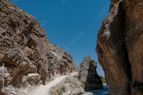 mountains of Central Asia. a narrow road between mountains. rapid river and sparse vegetation. there are no people.