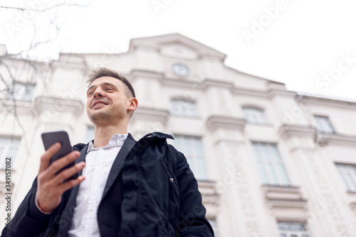 Smiling young male standing with smartphone outdoors