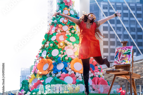 Street female artists feel happy, jumping and hand up in a modern city, big Christmas tree in background © chomplearn_2001