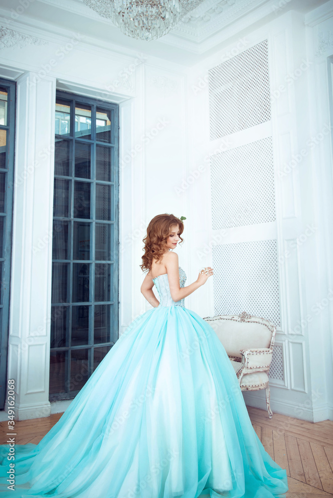The beautiful young girl the princess in a long magnificent turquoise dress stands in a light castle. Fairytale fashion photo session Cinderella. Beautiful room. Princess runs at the door The beautiful young girl the princess in a long magnificent turquoise dress stands in a light castle. Fairytale fashion photo session Cinderella. Beautiful room. Princess runs at the door