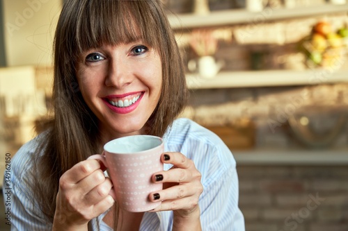 Closeup portrait of happy white woman at home drinking coffee at morning in kitchen.