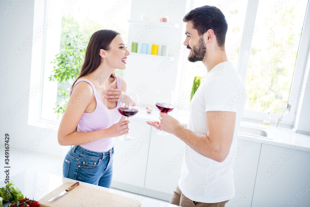 Profile side photo of positive cheerful man woman married couple stay home kitchen hold glass wine enjoy meal date tell speak laugh in house indoors Profile side photo of positive cheerful man woman married couple stay home kitchen hold glass wine enjoy meal date tell speak laugh in house indoors