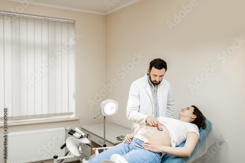 Doctor listening to a pregnant woman s belly with a stethoscope during a medical examination. Concept of medical care and health during a pregnancy