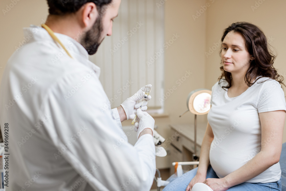 Doctor holding vaccine or some medication in the syringe, preparing for injection for a pregnant woman during a medical procedure in the clinic Doctor holding vaccine or some medication in the syringe, preparing for injection for a pregnant woman during a medical procedure in the clinic