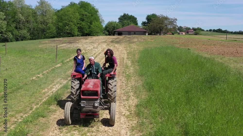 Farmer with apprentice riding tractor in farmland Farmer with apprentice riding tractor in farmland