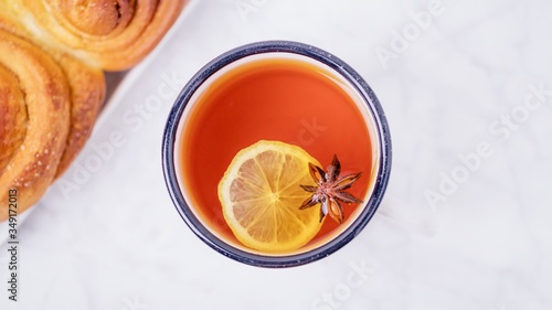 A cup of lemon tea with anise star and homemade cinnabons, cinnamon rolls buns on white marble background, panoramic format