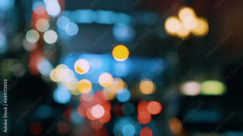 Rain flows on the front windshield glass window of car. Wipers moving. Beautiful colorful blurry rounded lights of traffic. Broken heart, sad, cry scene Rain flows on the front windshield glass window of car. Wipers moving. Beautiful colorful blurry rounded lights of traffic. Broken heart, sad, cry scene
