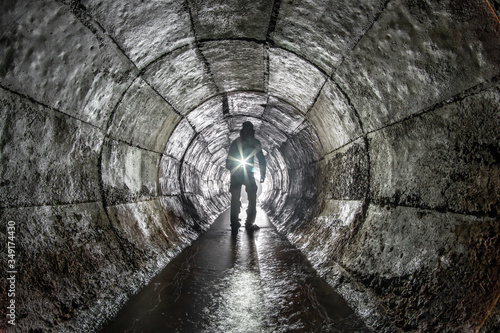 Man with a lantern in an underground round concrete rain collector.