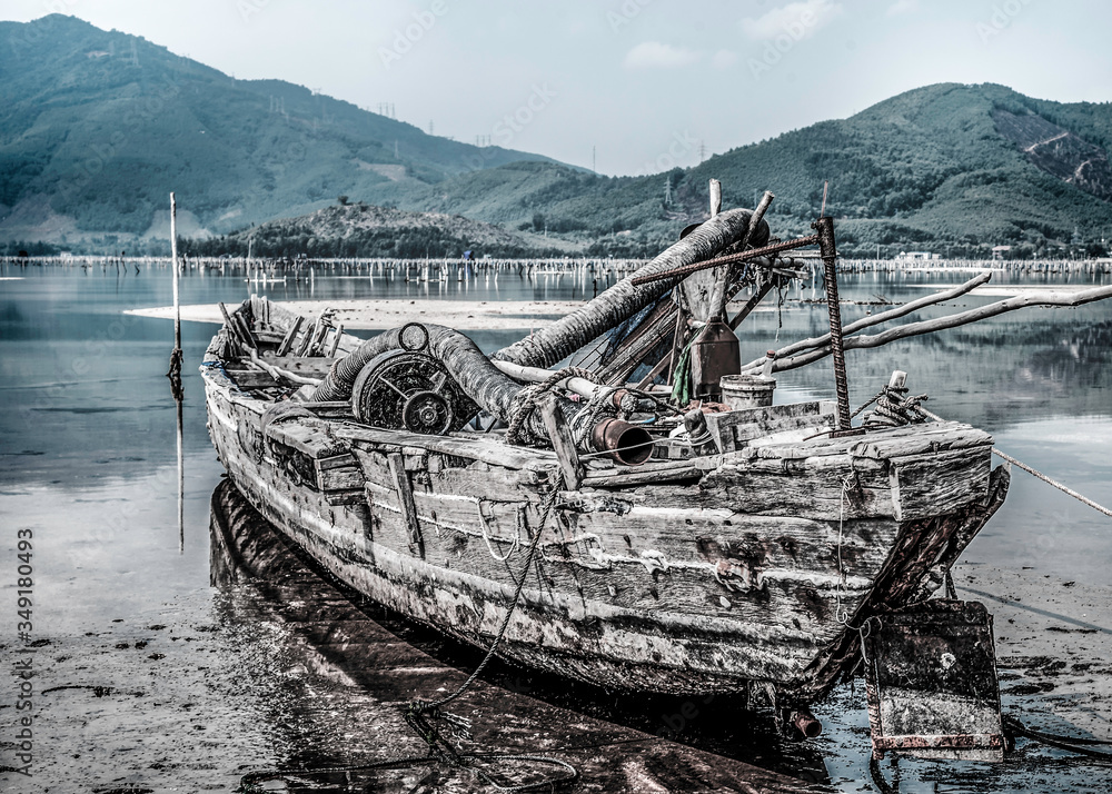 Old boat filled with trash standing on the seashore with mountains on background