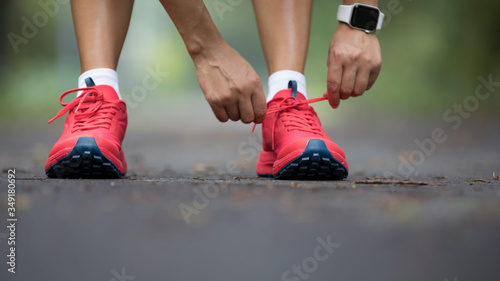 Female runner tying shoelace before running on park trail © lzf
