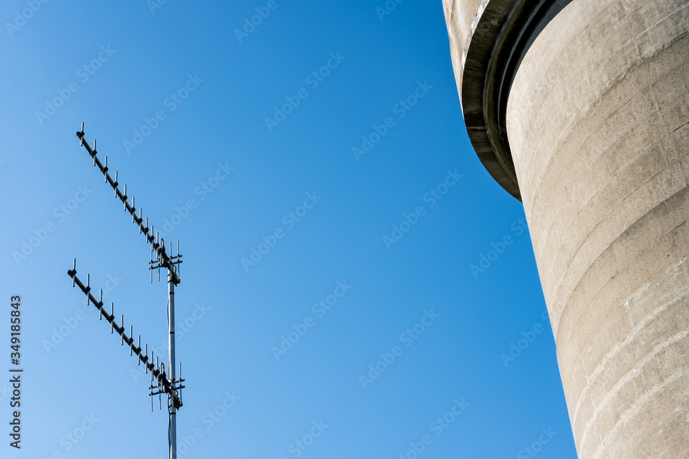 Abstract view of a cast concrete water tower and telecoms tower seen against a crisp sky. Nearby telemetry antennas are seen pointing to a remote control station during 5G tria Abstract view of a cast concrete water tower and telecoms tower seen against a crisp sky. Nearby telemetry antennas are seen pointing to a remote control station during 5G tria
