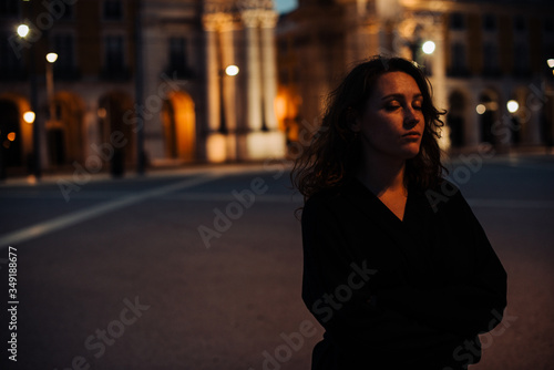 Half length portrait of woman wearing black, standing alone in the street with contemplative face expression, eyes closed. Night time, street light. Safety concept, night life or loneliness concept